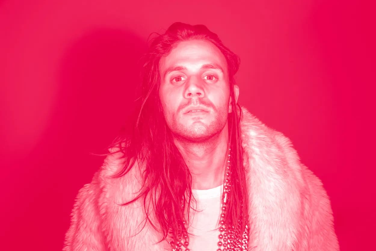 A man with long hair in a fur coat against hot pink