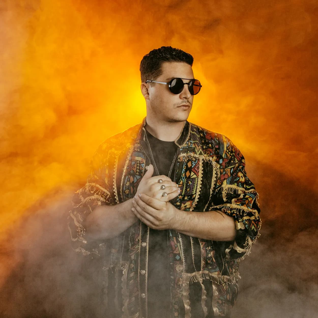 A man in sunglasses and a patterned jacket in orange smoke