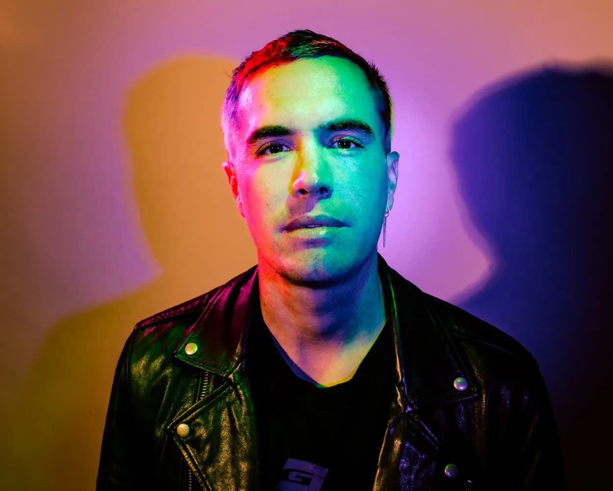A man in a leather jacket with colored shadows falling across his face