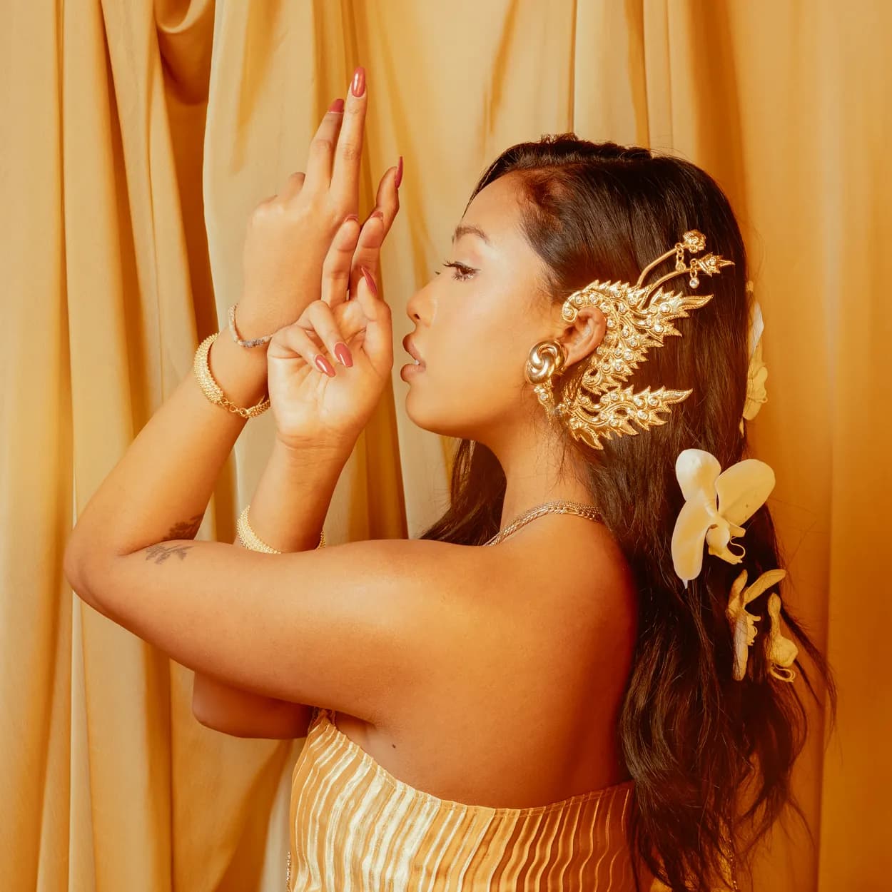 A woman in a gold hairpiece against warm orange curtains
