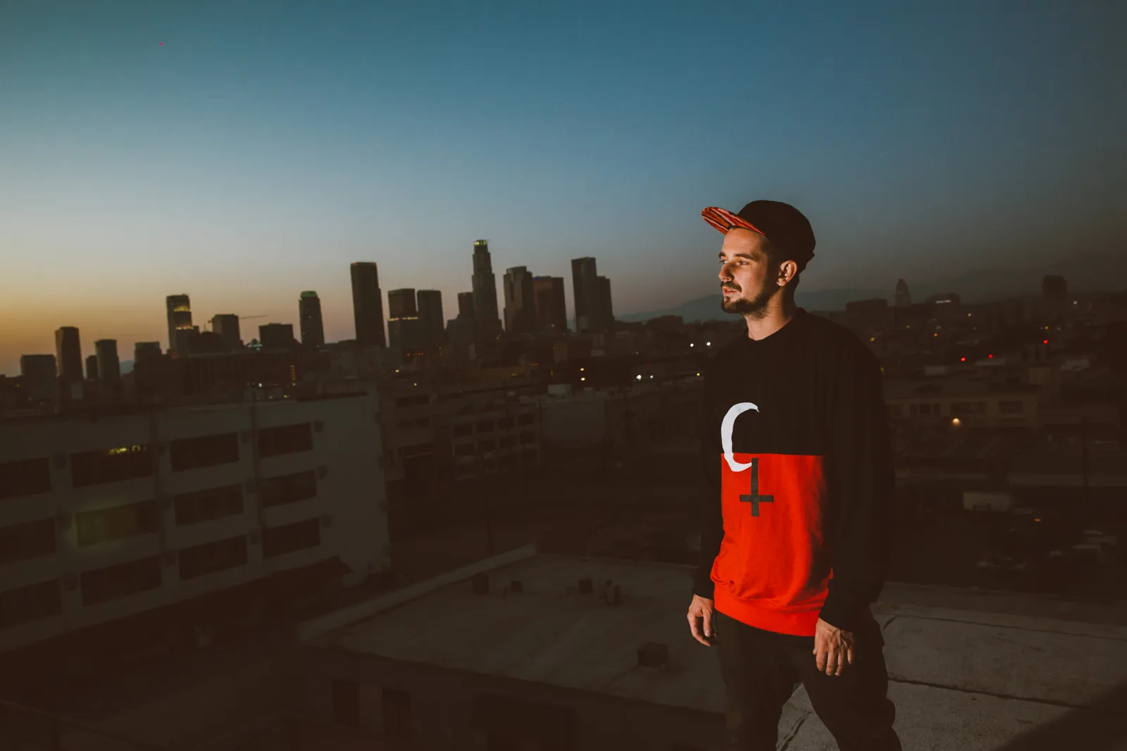 A man on a rooftop at dusk with the downtown Los Angeles skyline behind him