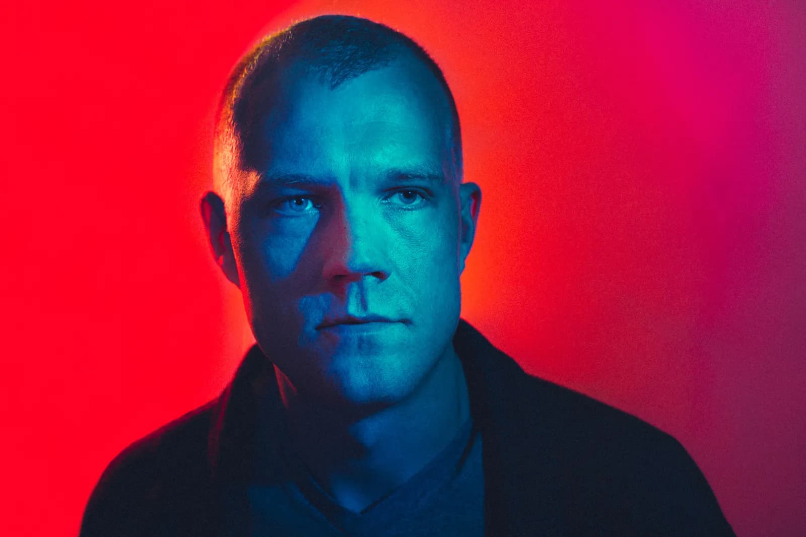 A man lit blue in front of a red backdrop