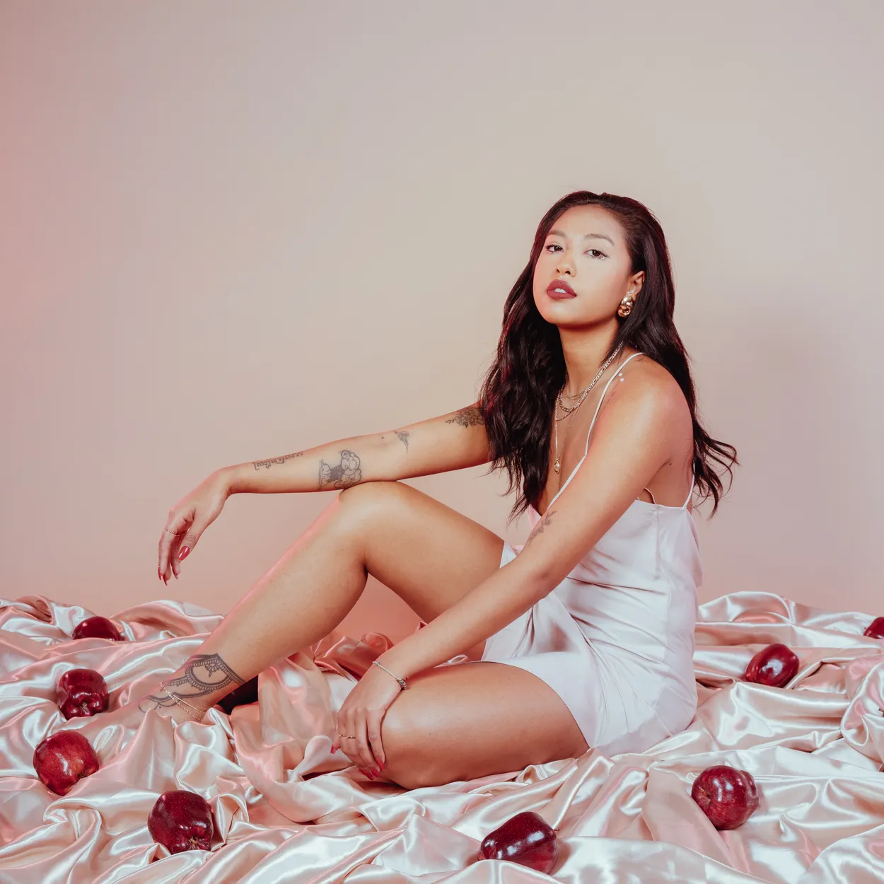 A woman seated on pink satin scattered with apples