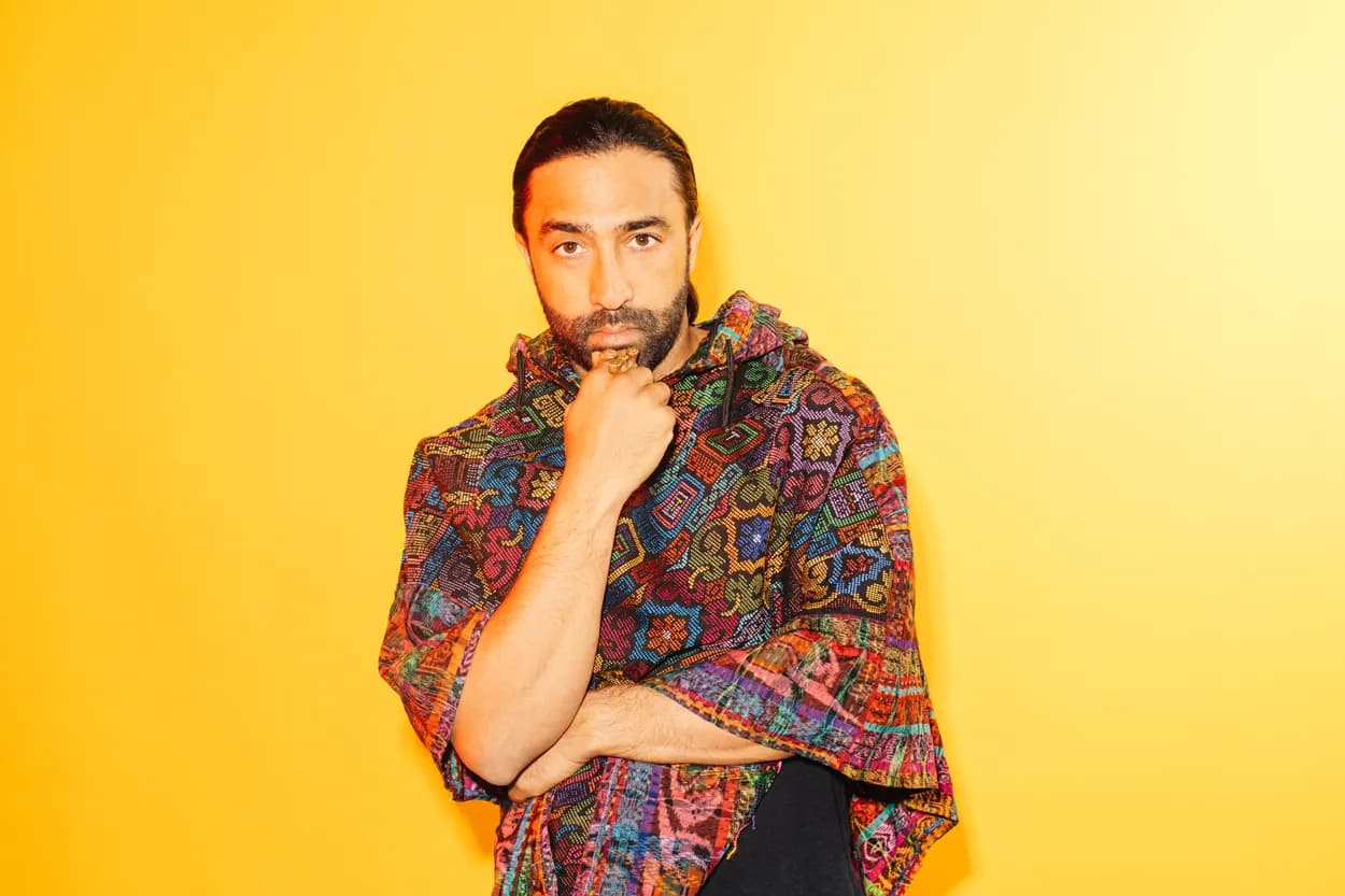 A man in a woven poncho against a yellow backdrop