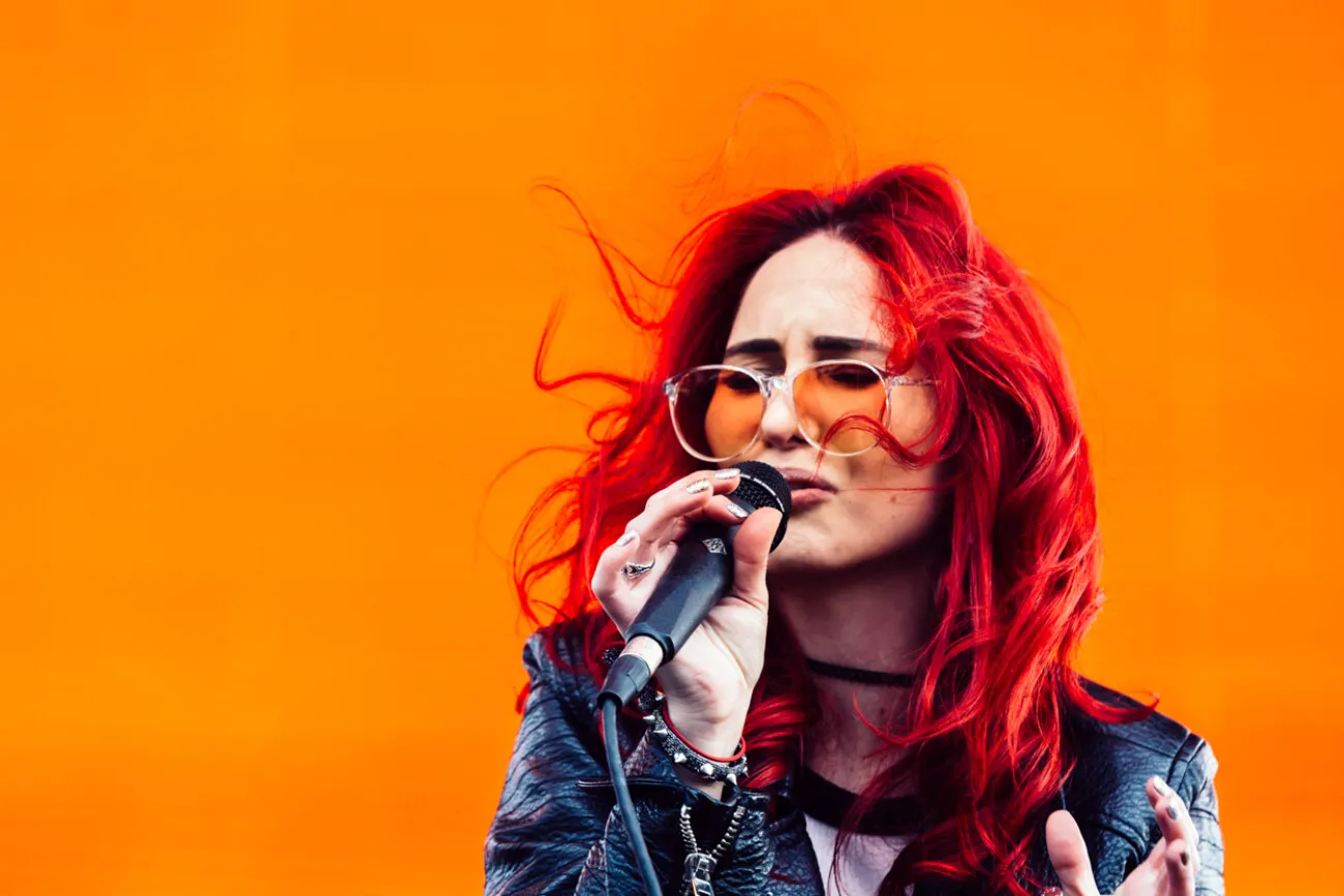 A singer with red hair at a microphone against orange