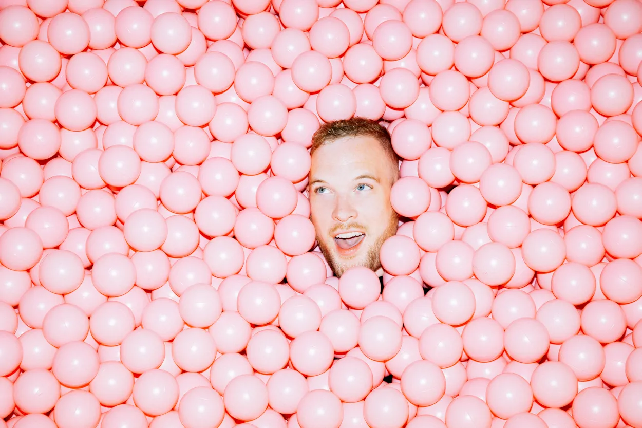 A man's face rising out of a pink ball pit